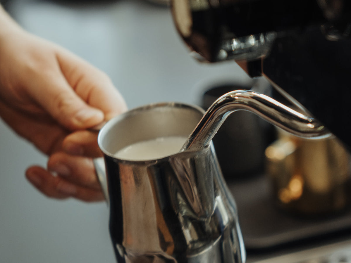 Titelbild zum Blogartikel über Milchschaum. Zu sehen ist ein gefülltes Milchkännchen an der Dampflanze einer Siebträgermaschine.