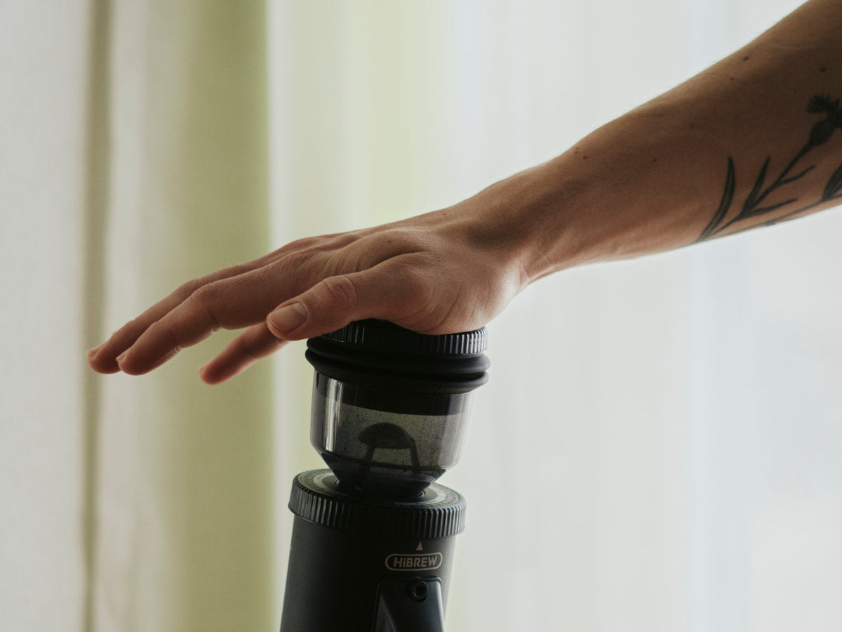 Hand drückt auf einen Blow Hopper einer Kaffeemühle. Titelbild des Beitrags.