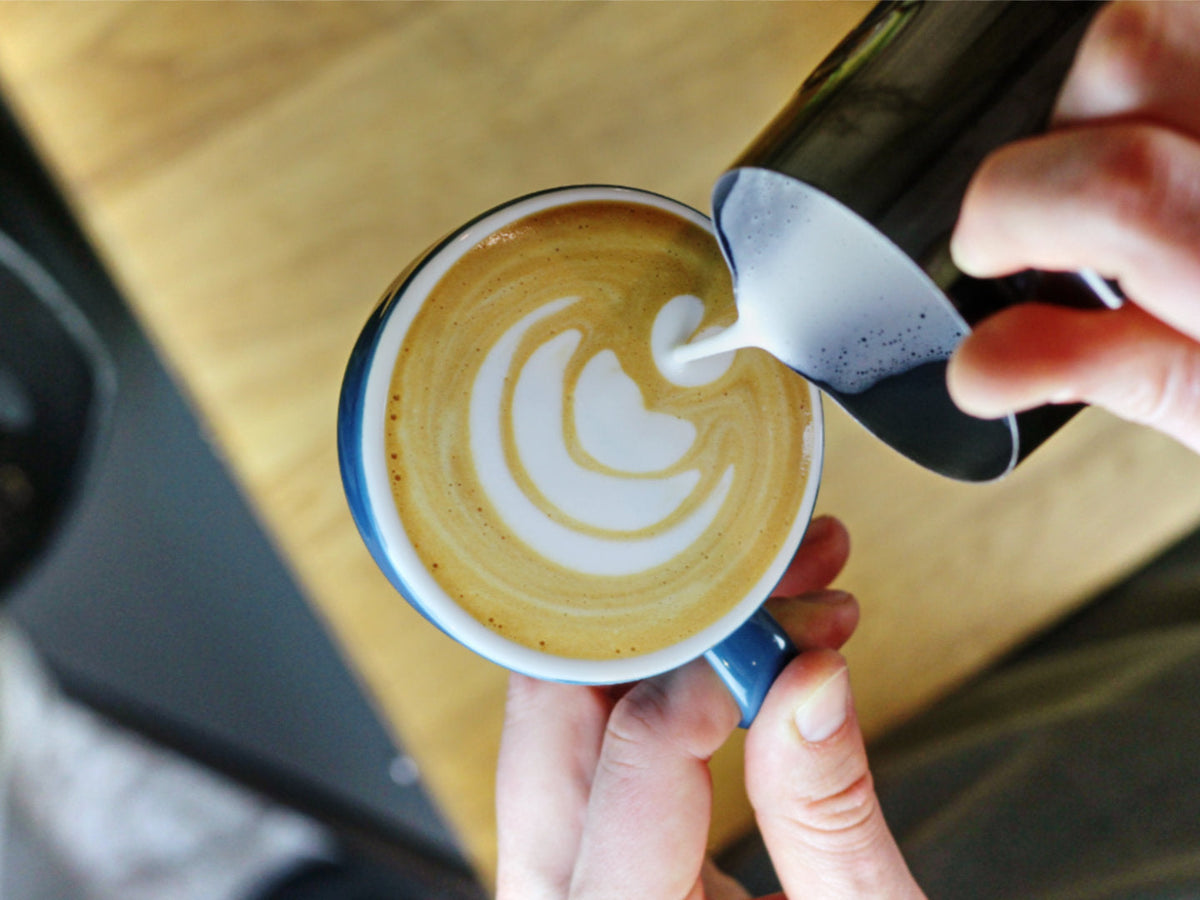 Titelbild zum Blogartikel über Latte Art. Zu sehen ist, wie Mats eine Tulpe in einen Espresso gießt. 